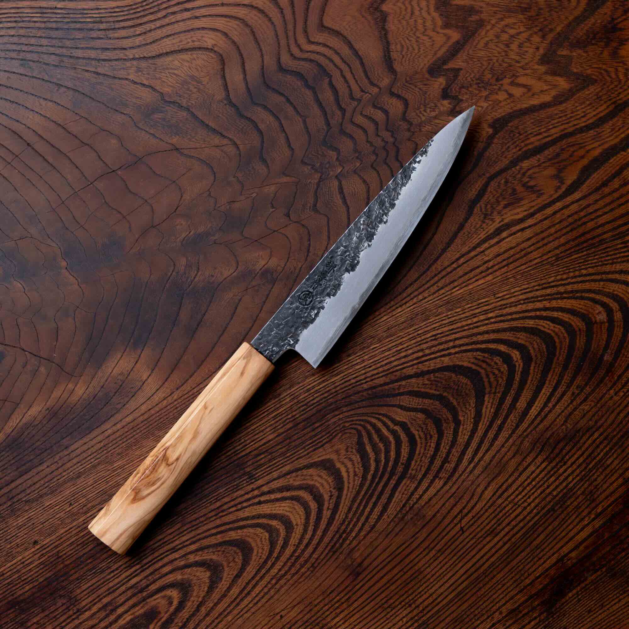 a rustic black blade with olive wood handle is laid on top of a dark wood background