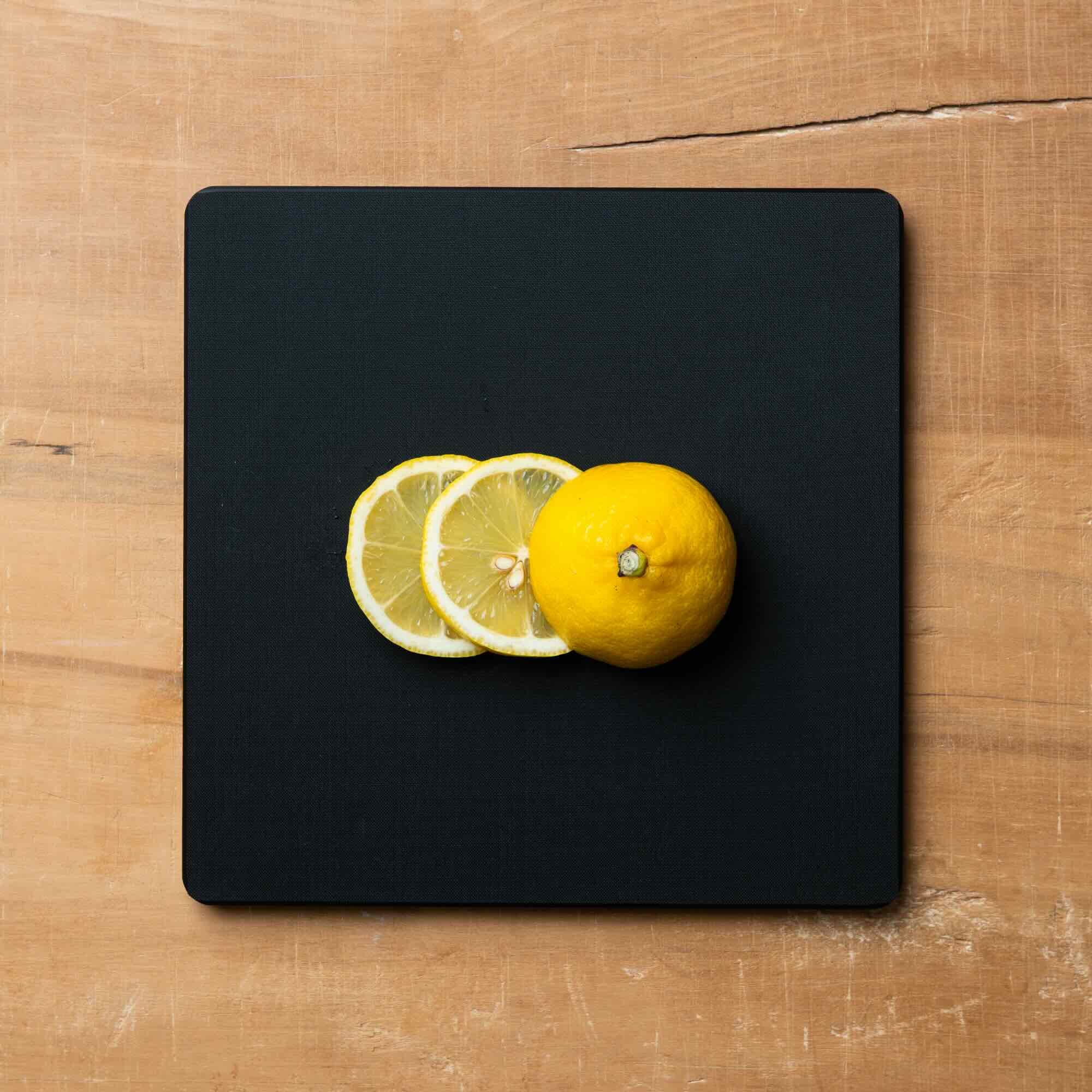 Lemons on a black square cutting board on a wooden surface