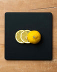 Lemons on a black square cutting board on a wooden surface