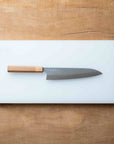 Chef's knife with wooden handle on a white cutting board over a wooden surface